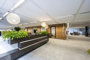 Modern office interior at Jacob Bontiusplaats with a plant-decorated reception desk, wooden wall panels, and open workspace.